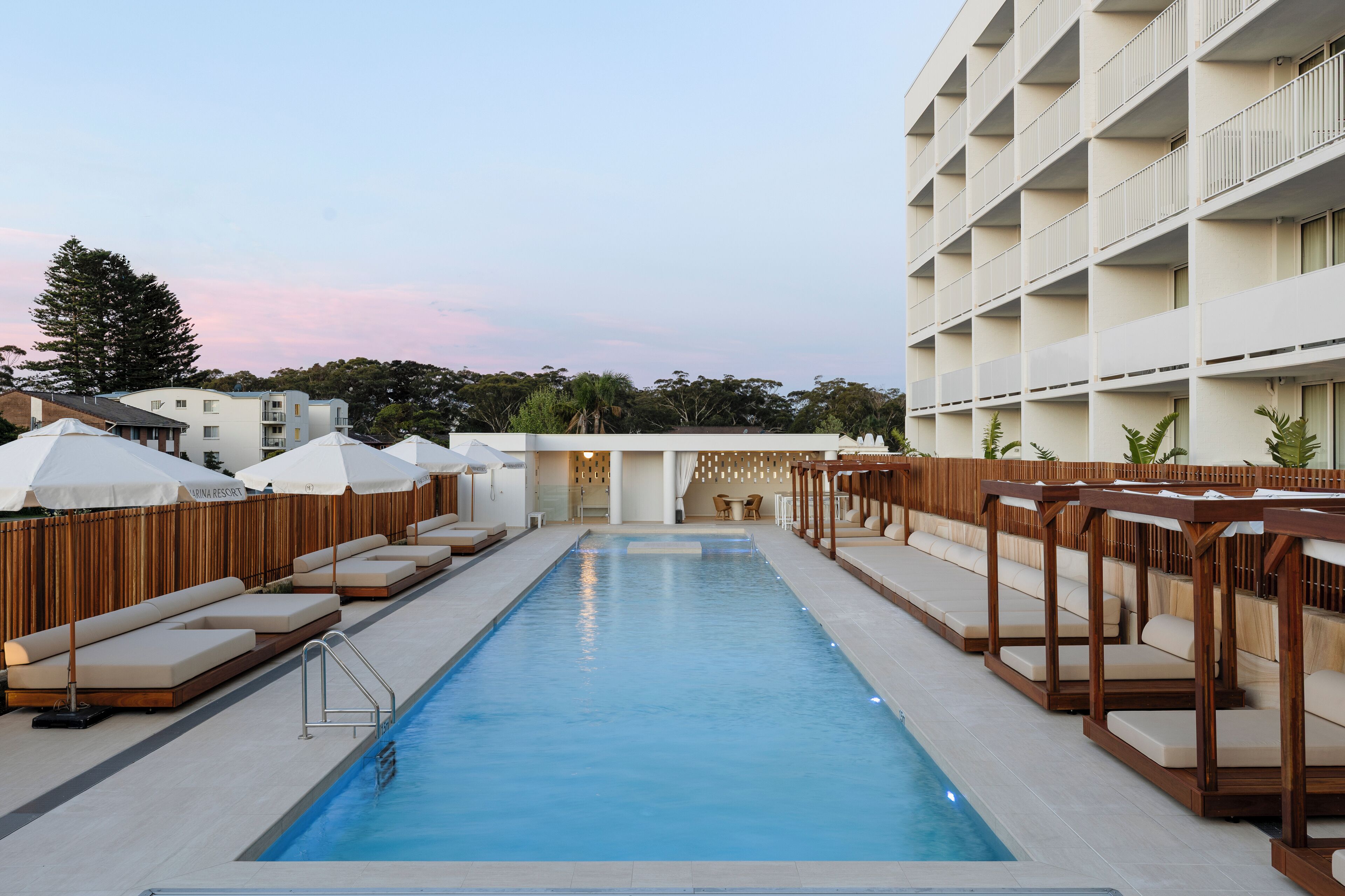 A swimming pool with lounge chairs and umbrellas, surrounded by a building with multiple balconies.