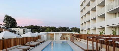 A swimming pool with lounge chairs and umbrellas, surrounded by a building with multiple balconies.