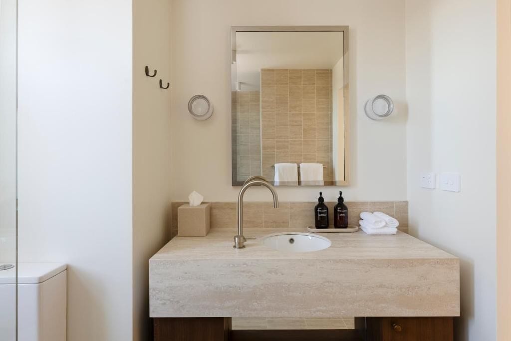 A modern bathroom with a beige marble sink, a large mirror, and two towel dispensers.