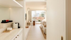 A modern hotel room with a large bed, a sitting area with a sofa and a coffee table, a kitchen area with a countertop and a sink, and a view of the outside through large windows. - Marina Resort - Adults Only (Nelson Bay)