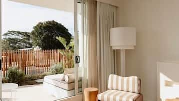 A hotel room with a large sliding glass door leading to a balcony, a striped armchair, a bedside table, and a lamp.