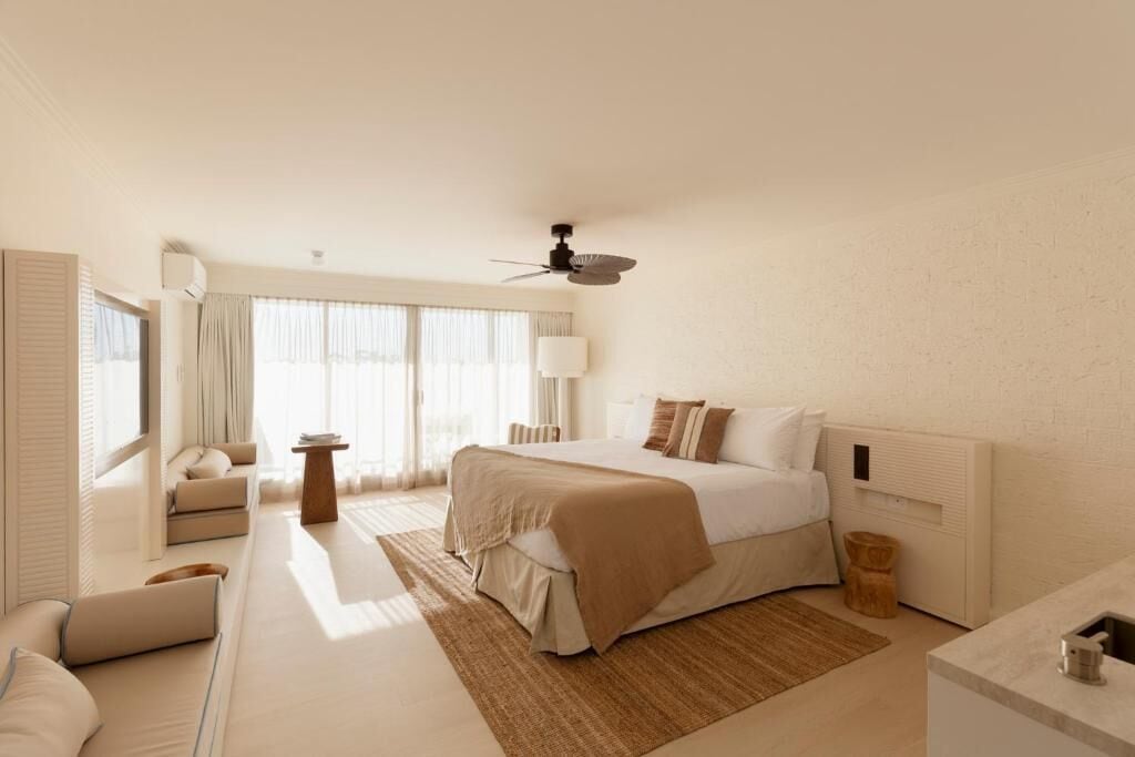 A modern hotel room with a large bed, a sofa, a small table, and a ceiling fan.
