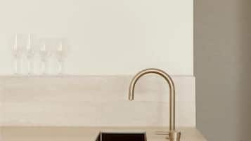 Cocina minimalista con encimera blanca, grifo dorado y un juego de copas de vino en la pared.