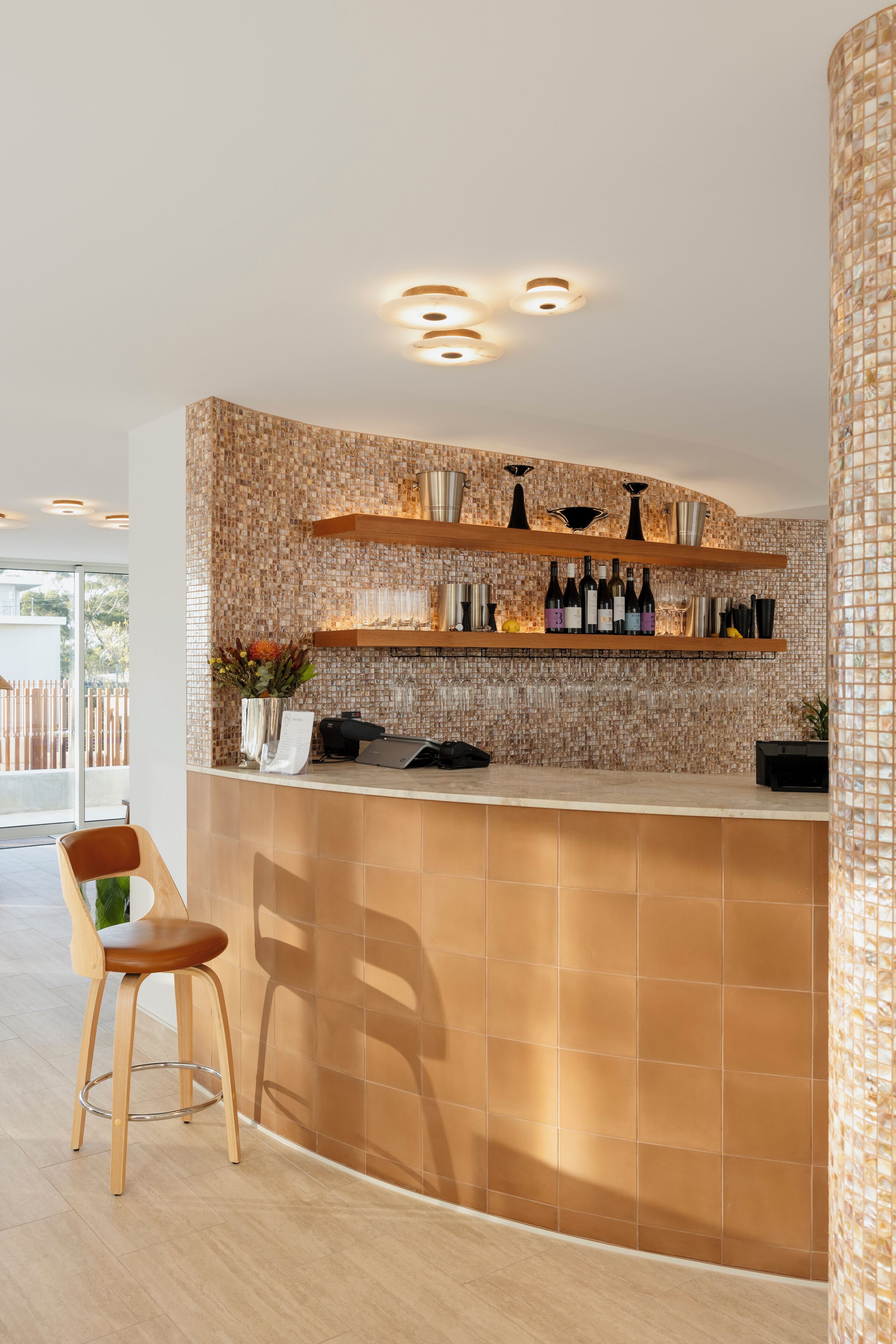 A modern bar area with a curved counter, wooden shelves, and a patterned wall.
