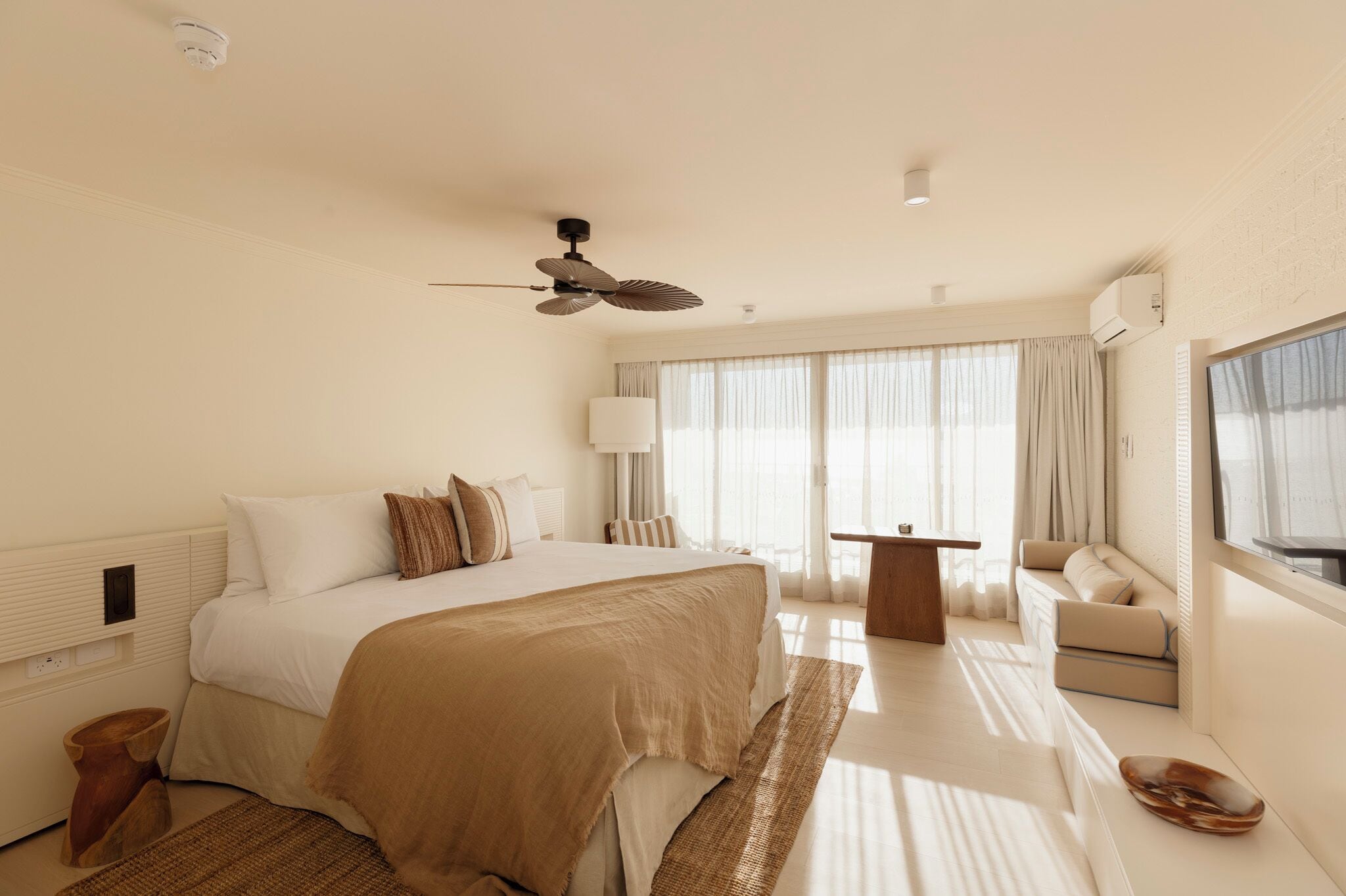 Ein Hotelzimmer mit einem großen Bett, einem Deckenventilator, einer Sitzecke mit Sofa und Sesseln, einem kleinen Tisch und einem Fenster mit Vorhängen.