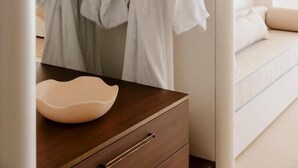 A modern bedroom with a bed, a wooden dresser, and two white bathrobes hanging on a rack. - Marina Resort - Adults Only (Nelson Bay)