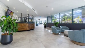 Um hall moderno com balcão de recepção, área de estar e grandes janelas com vista para o exterior.