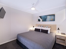 A bedroom with a bed, a nightstand, a lamp, a ceiling fan, and a painting on the wall.