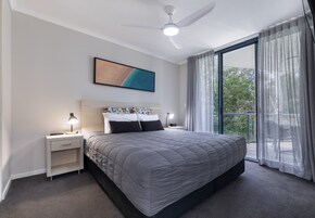 Un dormitorio moderno con una cama grande, lámparas de noche, ventilador de techo y vistas amplias a través de un ventanal.