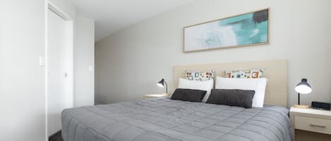 A neatly arranged hotel room with a large bed, two bedside tables with lamps, a wall-mounted painting, and a door to the left.