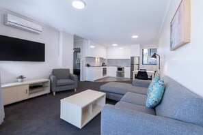 A modern living room with a grey sofa, a white coffee table, and a grey armchair. A flat-screen TV is mounted on the wall, and there is a small plant on a shelf. - The Landmark Resort Nelson Bay (Nelson Bay)