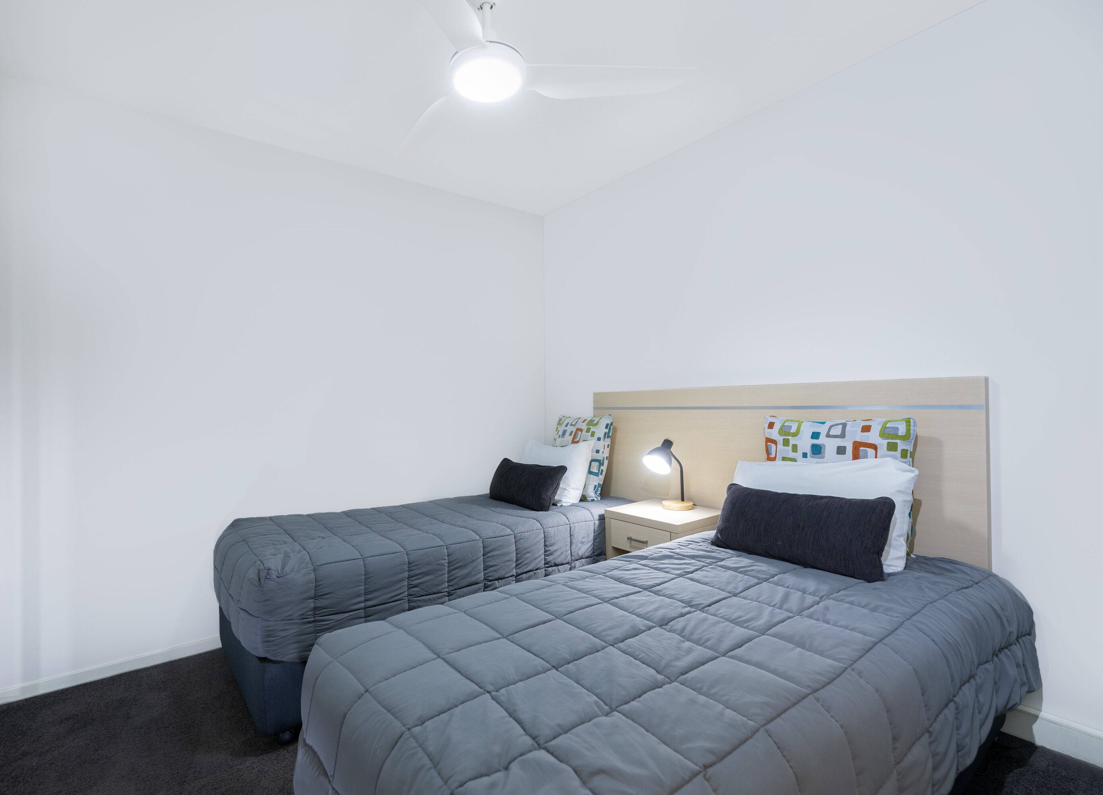 Ein Doppelzimmer mit zwei Betten, einem Nachttisch, einem Schreibtisch und einem Deckenventilator.