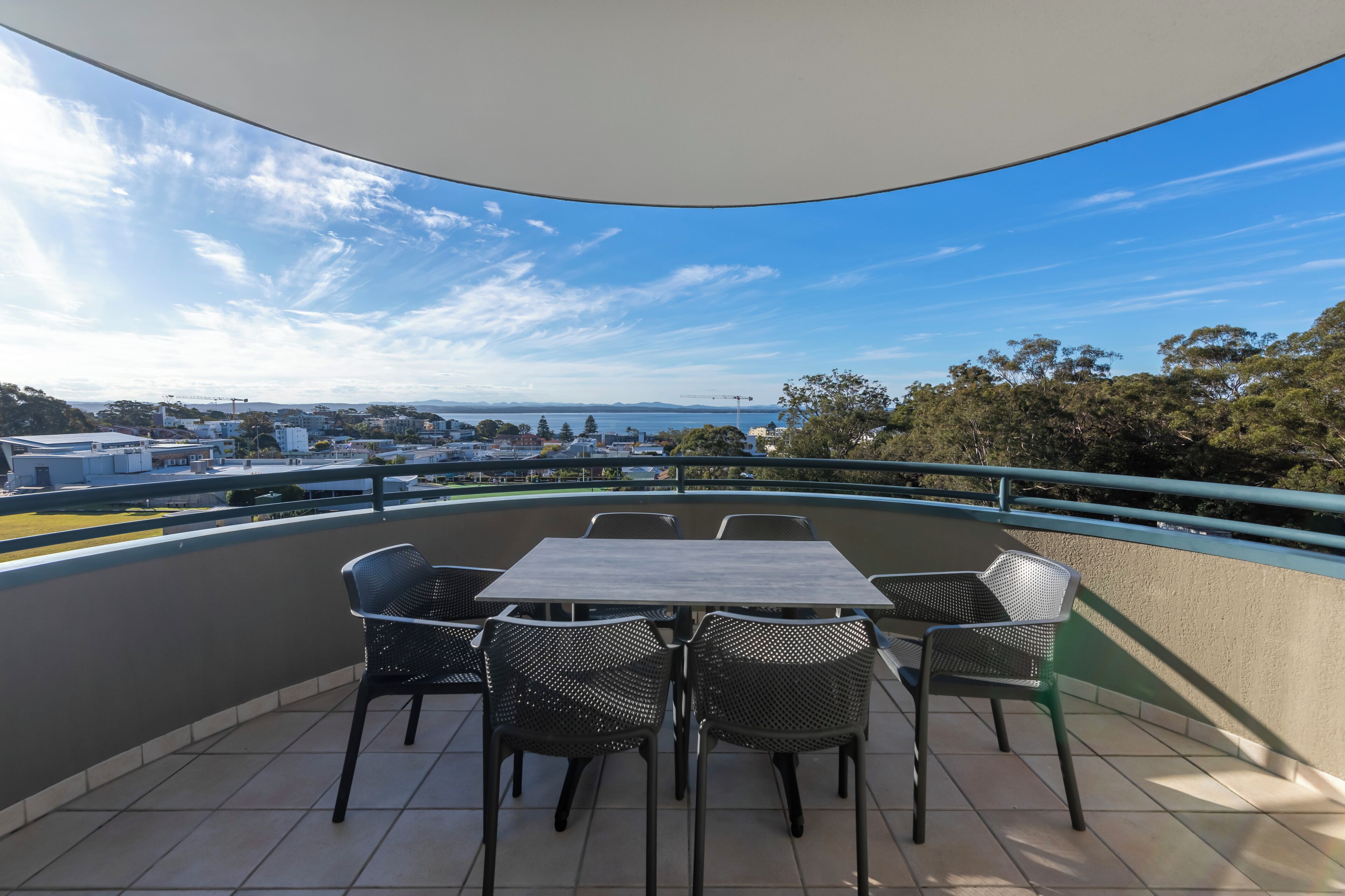 Un balcon avec une table et des chaises, offrant une vue sur le paysage urbain et une étendue d’eau.