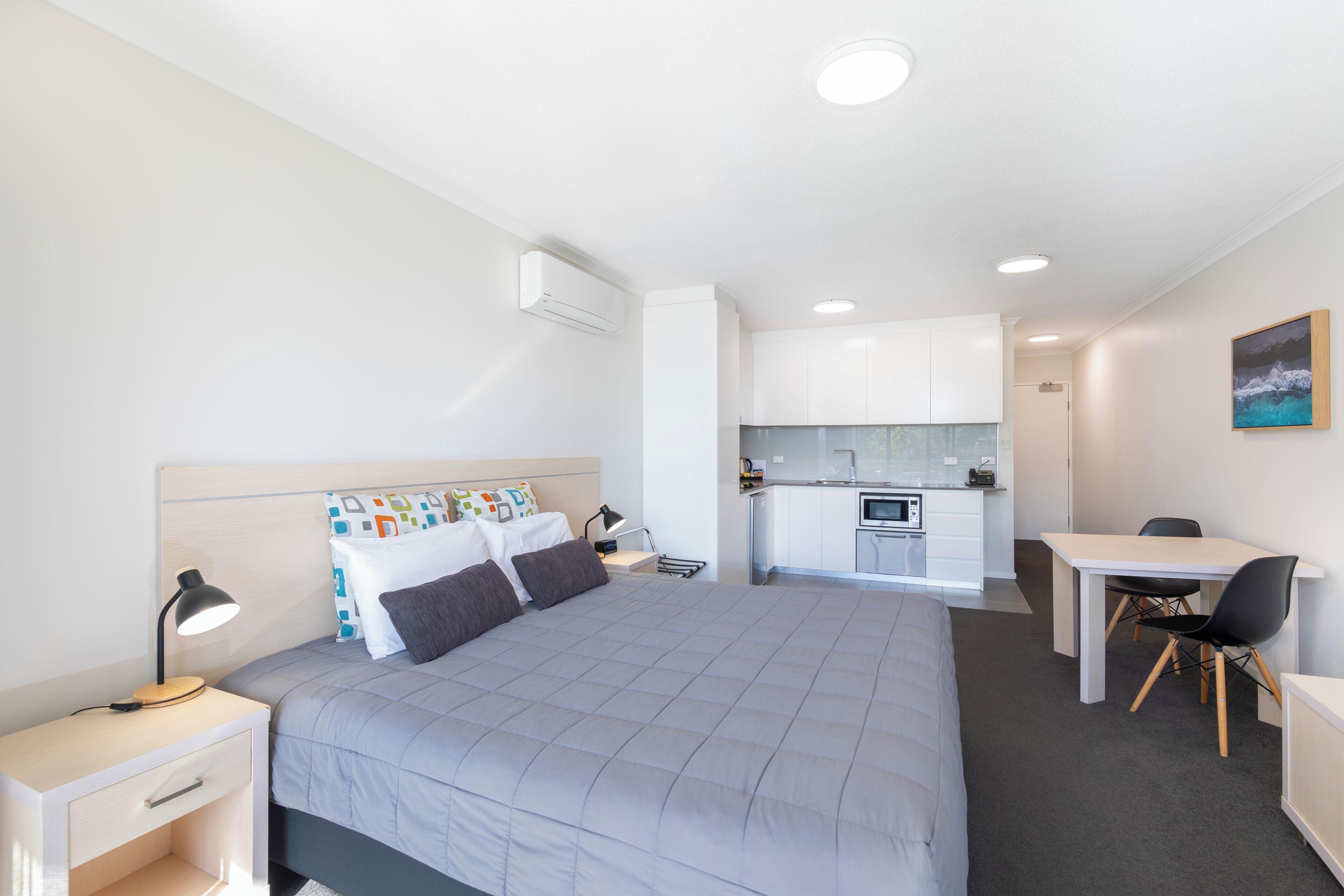 Una habitación de hotel moderna con una cama grande, un escritorio, una silla y una kitchenette.