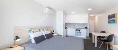Una habitación de hotel moderna con una cama grande, un escritorio, una silla y una kitchenette.