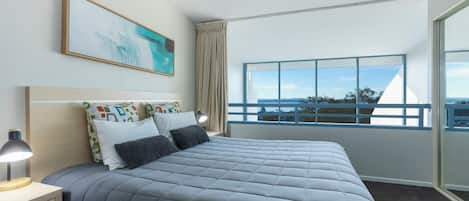 A modern hotel room with a large bed, a nightstand, a desk, and a window with a view of the city.