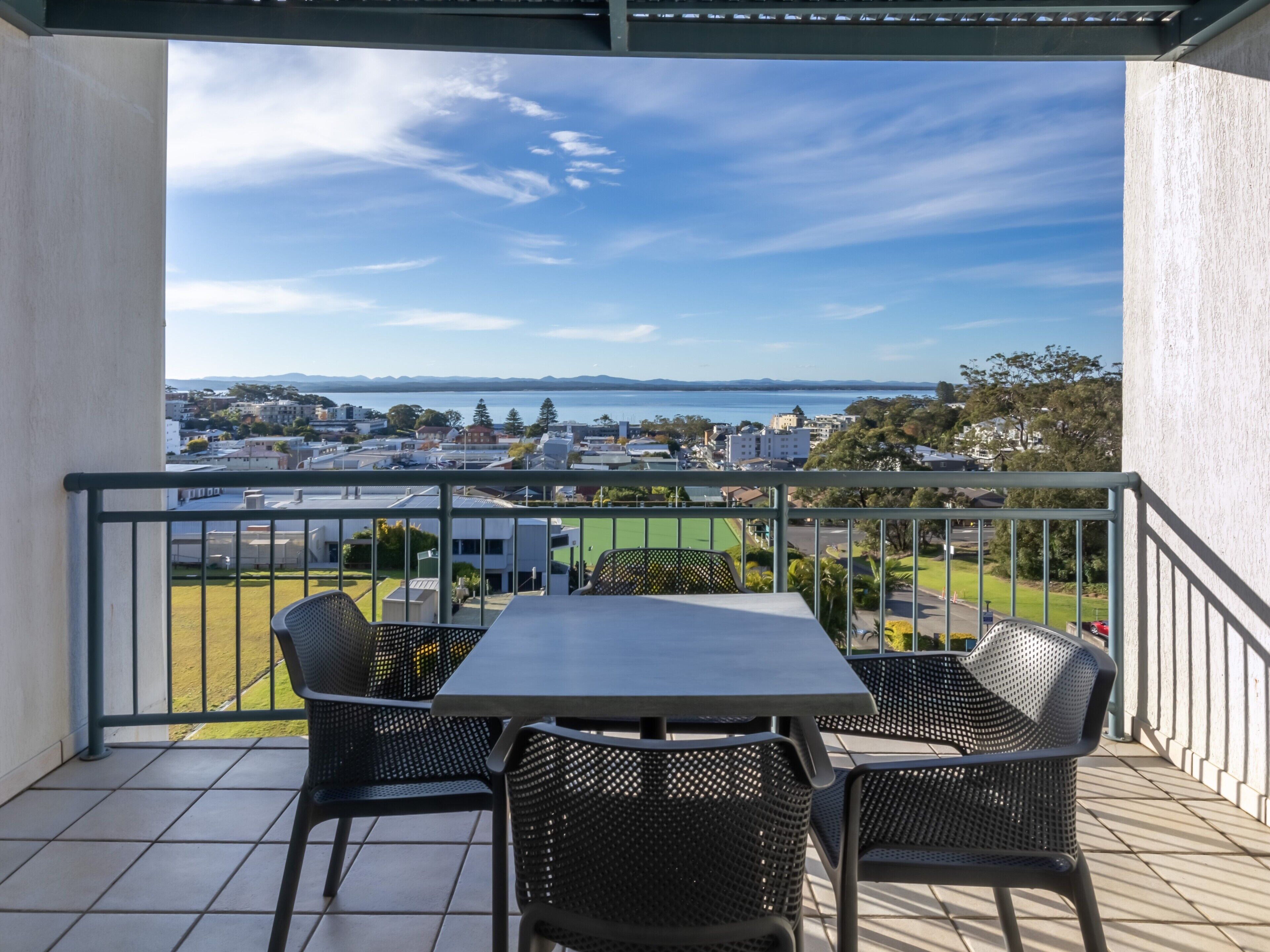 A balcony with a table and chairs, overlooking a residential area and a body of water.