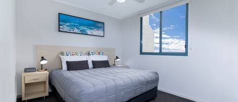 A bedroom with a bed, nightstands, a ceiling fan, a window with a view of the sky, and a painting on the wall.