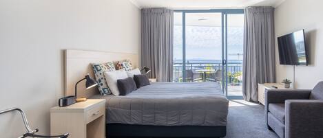 Una habitación de hotel moderna con cama, escritorio, silla, televisión y balcón con vistas.
