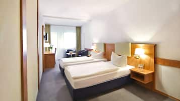 Une chambre d’hôtel avec trois lits, un bureau, une chaise et une table de chevet avec des lampes.