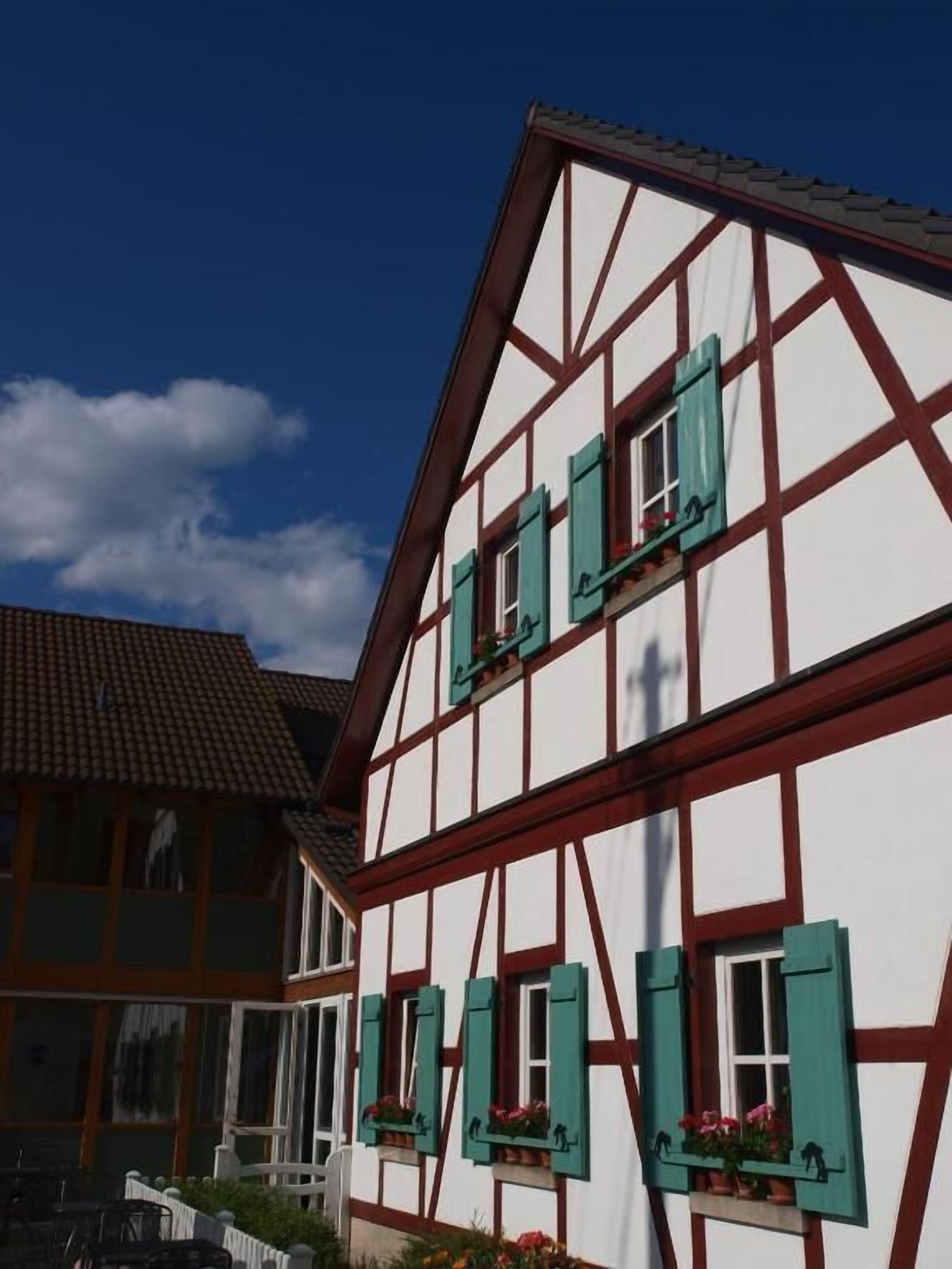 A traditional half-timbered building with multiple windows and shutters, a white facade, and a tiled roof.