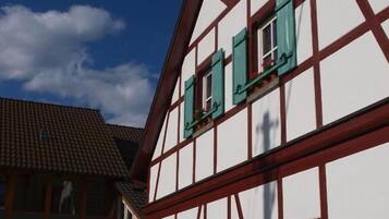 A traditional half-timbered building with multiple windows and shutters, a white facade, and a tiled roof.