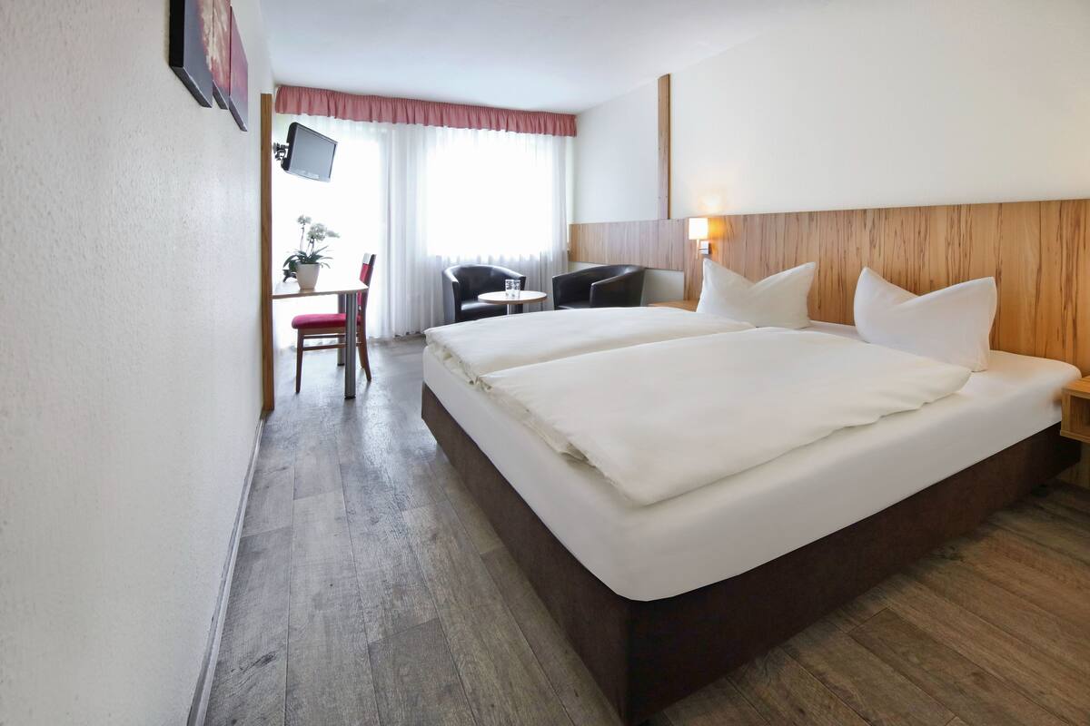 A hotel room with a large bed, two bedside tables, a desk with a chair, and a TV mounted on the wall.