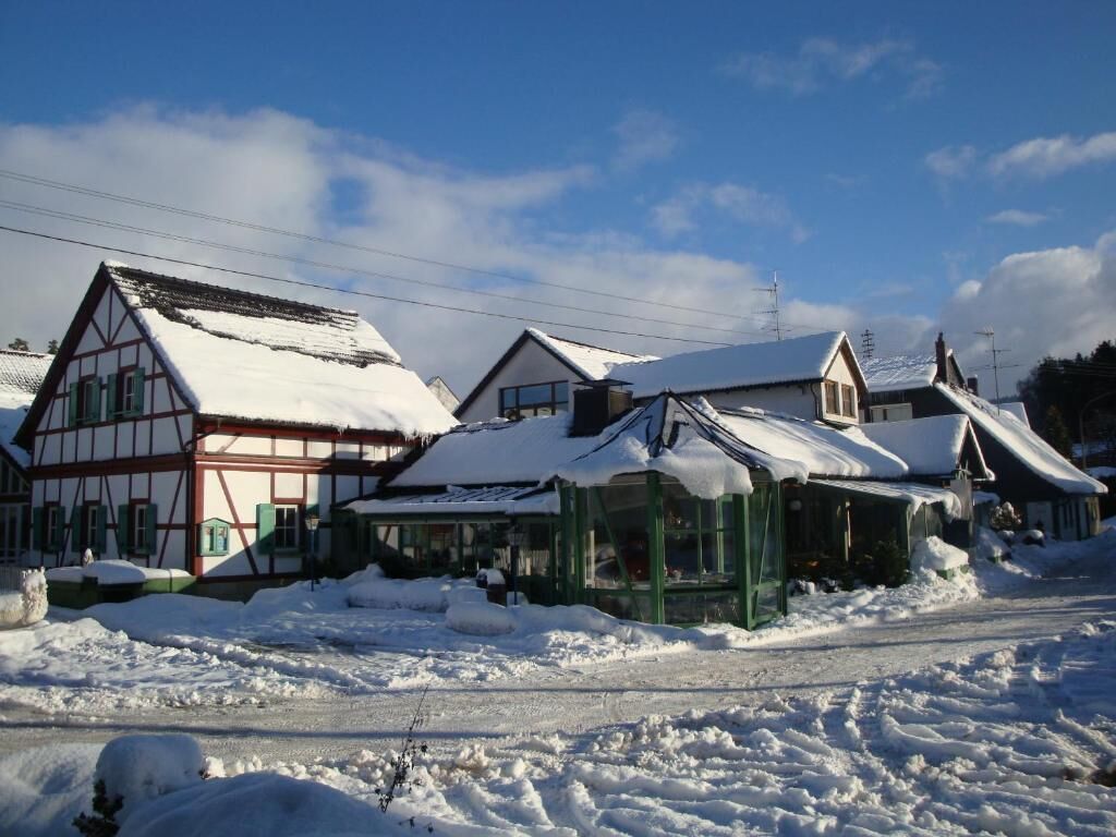 A traditional half-timbered house with snow-covered roofs and a green structure in the foreground.