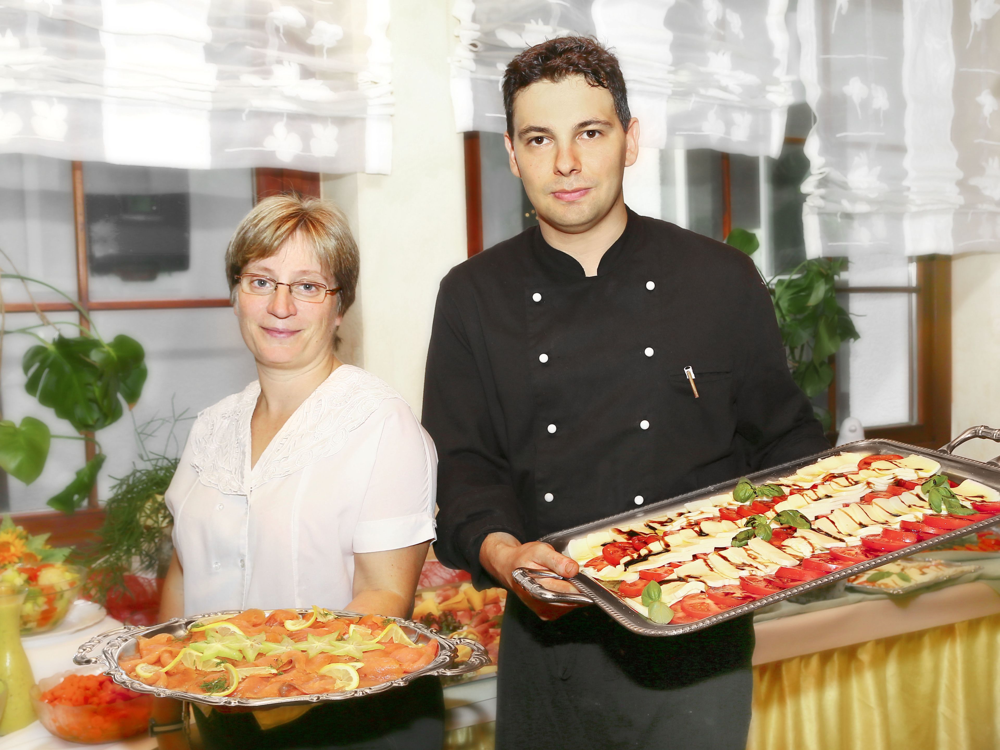 Two individuals holding trays of food, likely at a buffet or catering event.