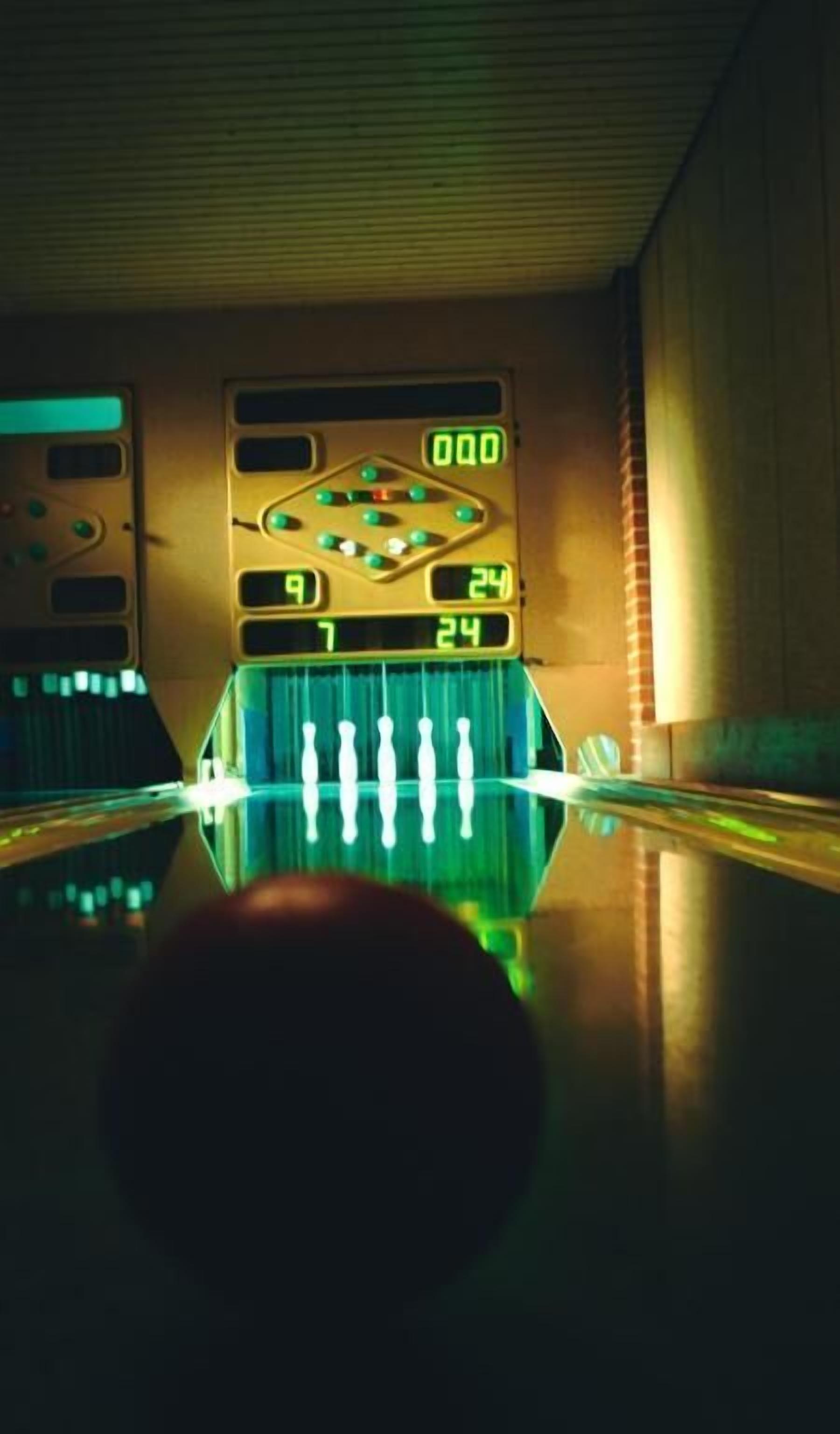 A bowling alley with a digital scoreboard displaying scores and a bowling ball in the foreground.