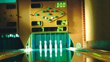 A bowling alley with a digital scoreboard displaying scores and a bowling ball in the foreground.