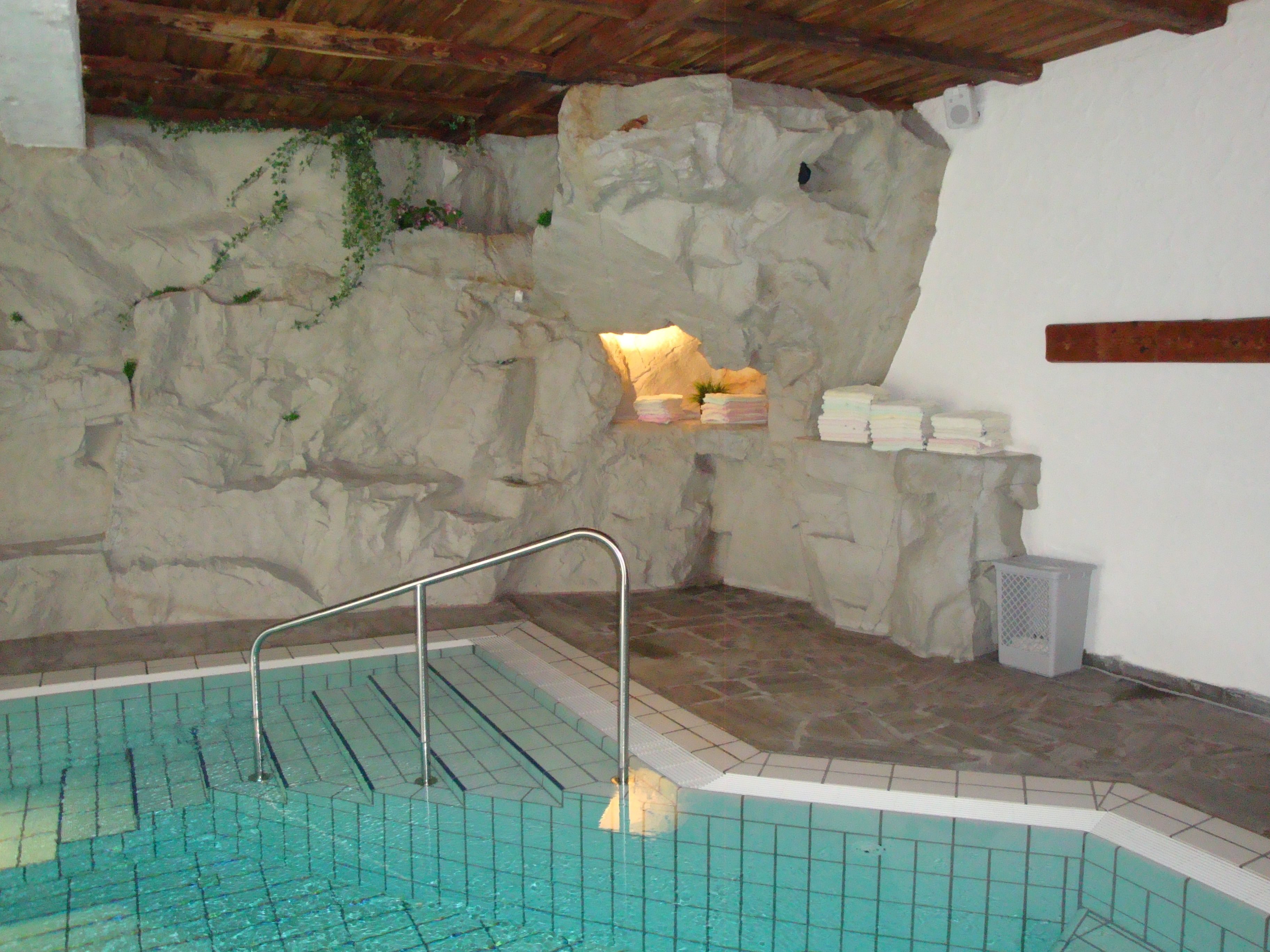 A stone-walled indoor pool with a tiled floor and a metal ladder.