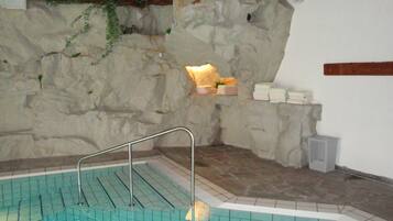 A stone-walled indoor pool with a tiled floor and a metal ladder.