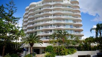 A multi-story hotel with balconies, palm trees, and a clear sky.