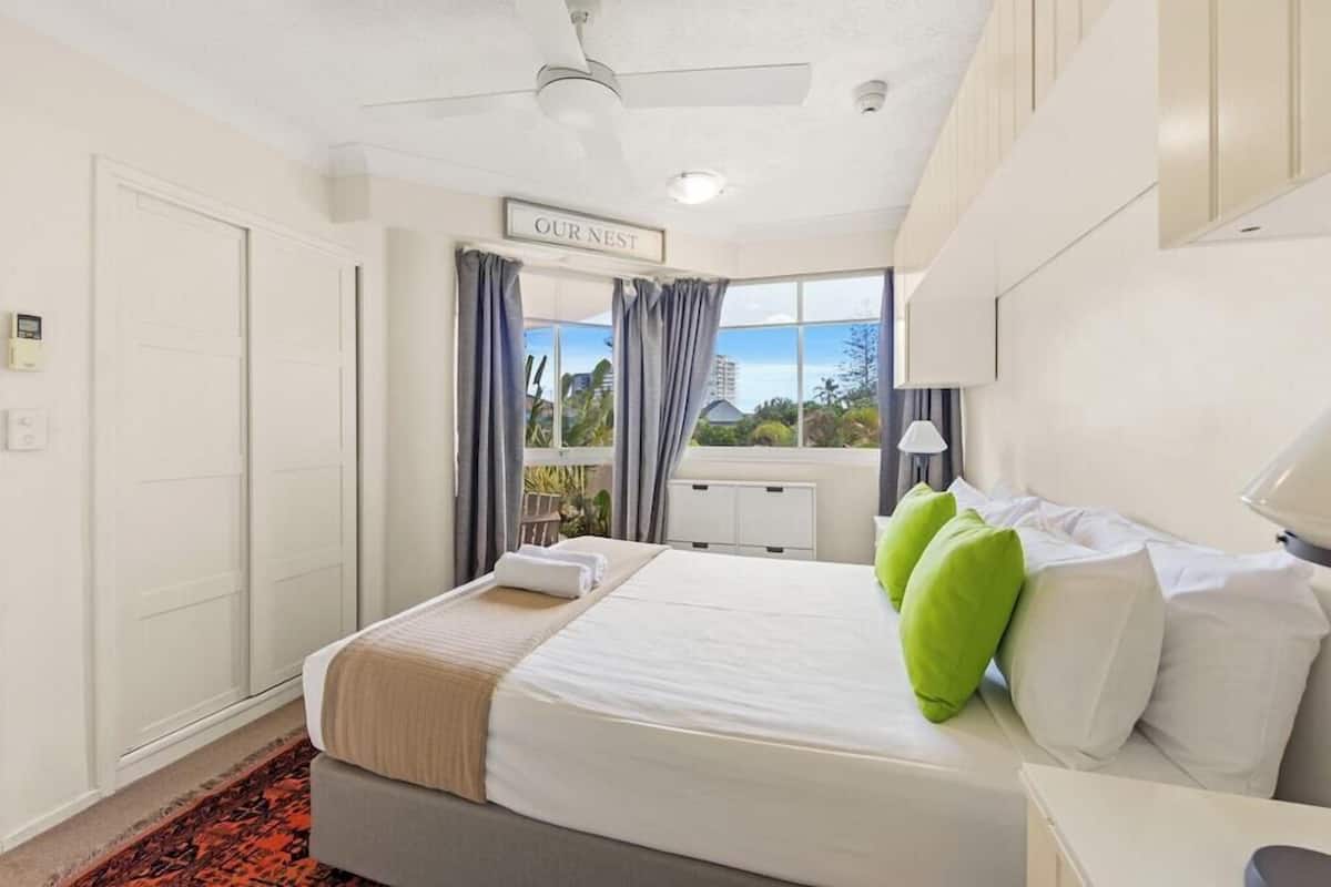 A hotel room with a bed, a ceiling fan, a view of the outdoors, and a sign that reads 'OUR NEST'.