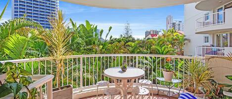 A balcony with a round table and chairs, surrounded by potted plants and a white railing.
