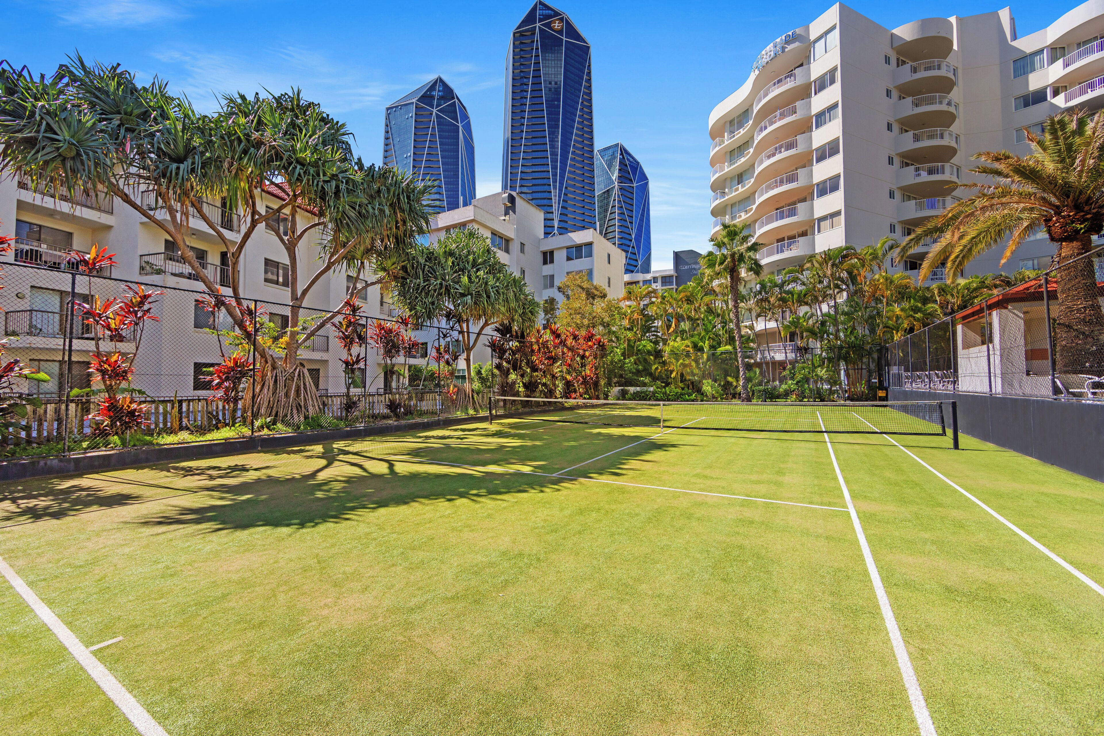 A tennis court surrounded by palm trees and buildings.
