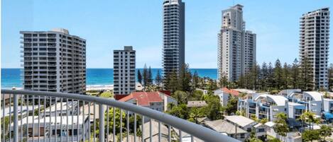 A coastal cityscape with high-rise buildings, a beach, and a residential area with a balcony view.