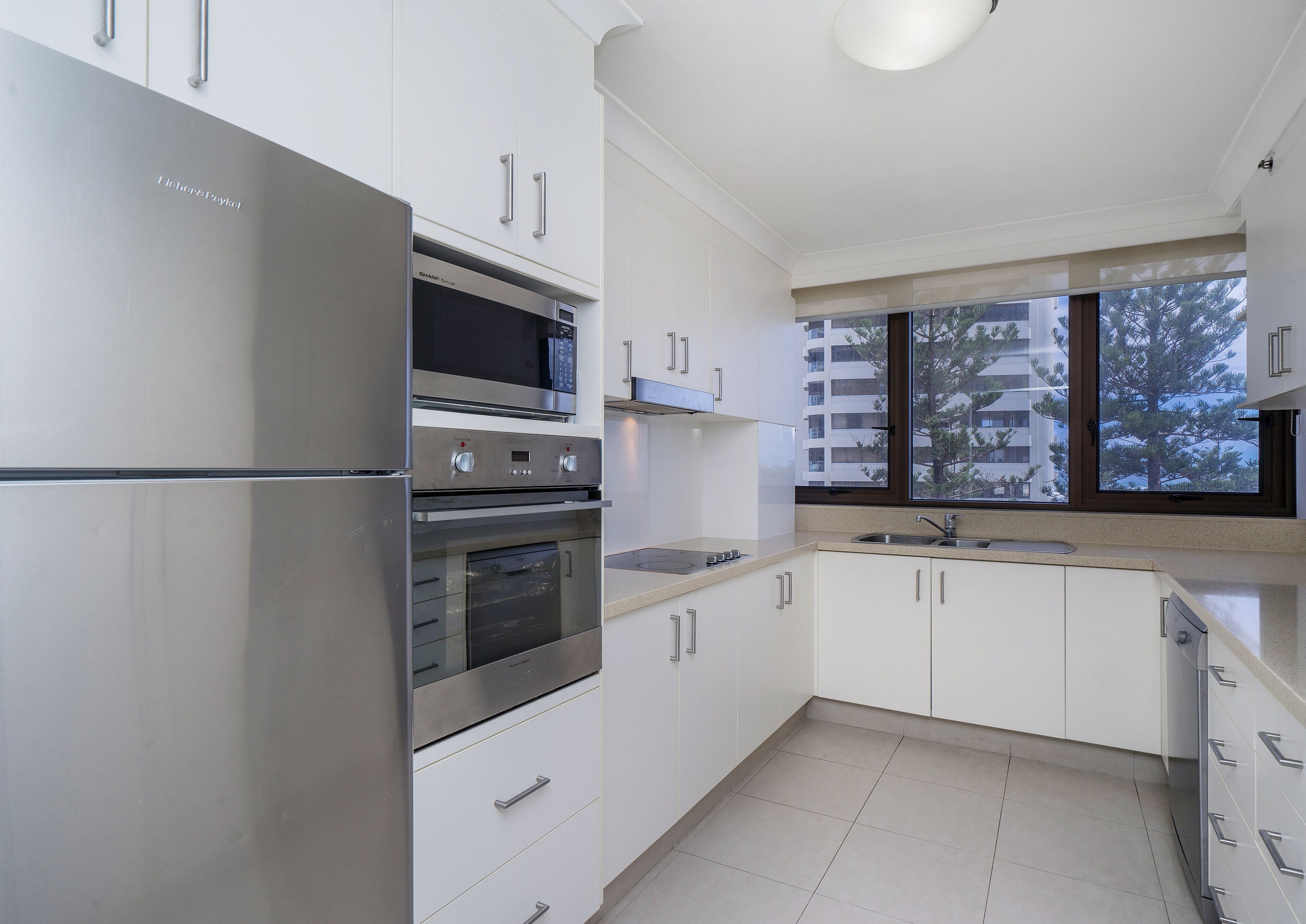 A modern kitchen with stainless steel appliances, white cabinetry, and a large window offering a view of the city.