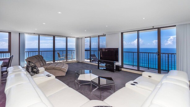 Un salón amplio con televisor grande, sofás blancos y un balcón con vista al océano.