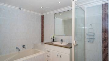 A bathroom with a bathtub, a sink, a mirror, and a shower area.