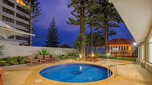 Una piscina de diseño circular, rodeada de mobiliario exterior y un edificio al fondo.