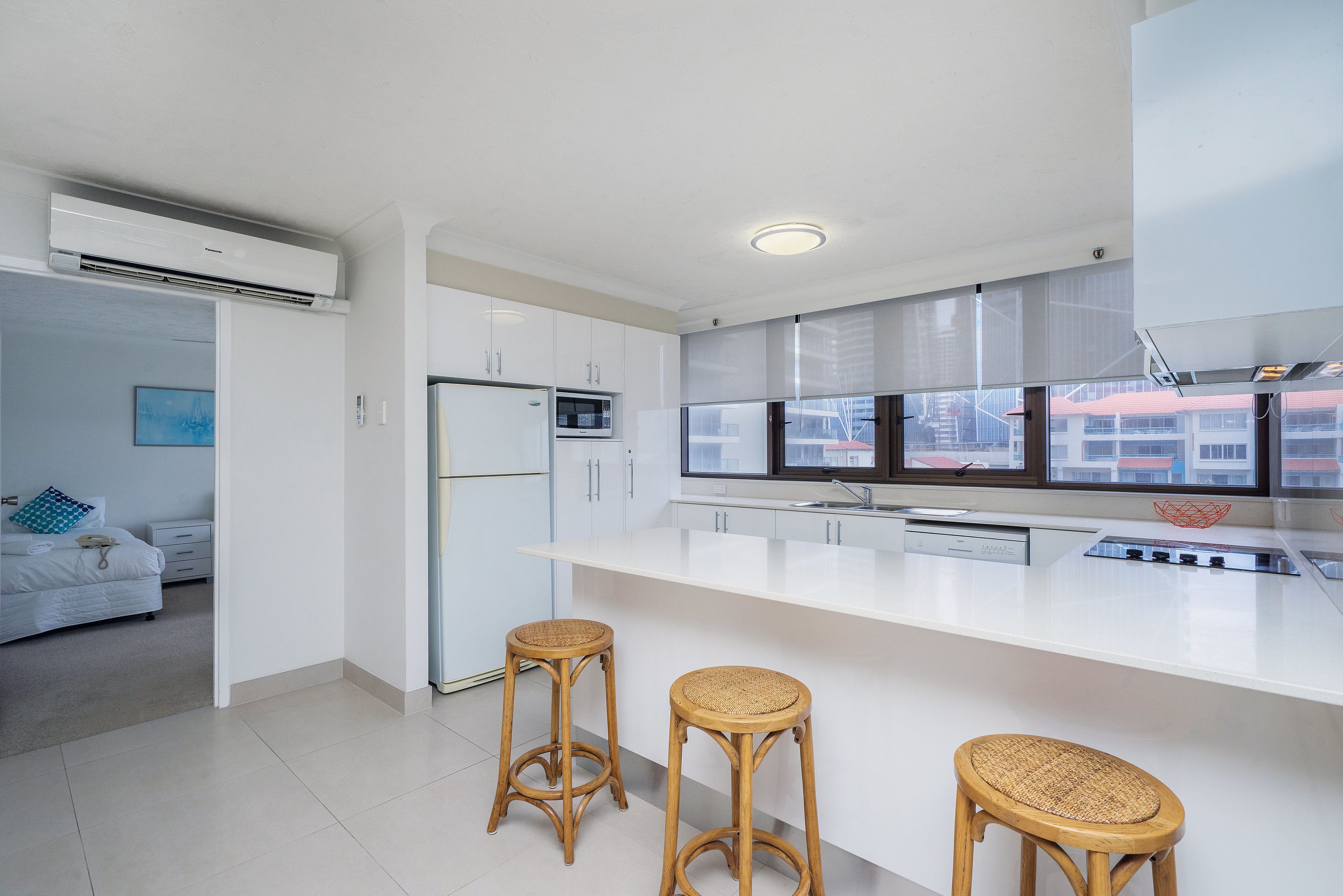 A modern kitchen with white cabinetry, a large island with stools, and a view through the window.