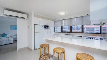 A modern kitchen with white cabinetry, a large island with stools, and a view through the window.