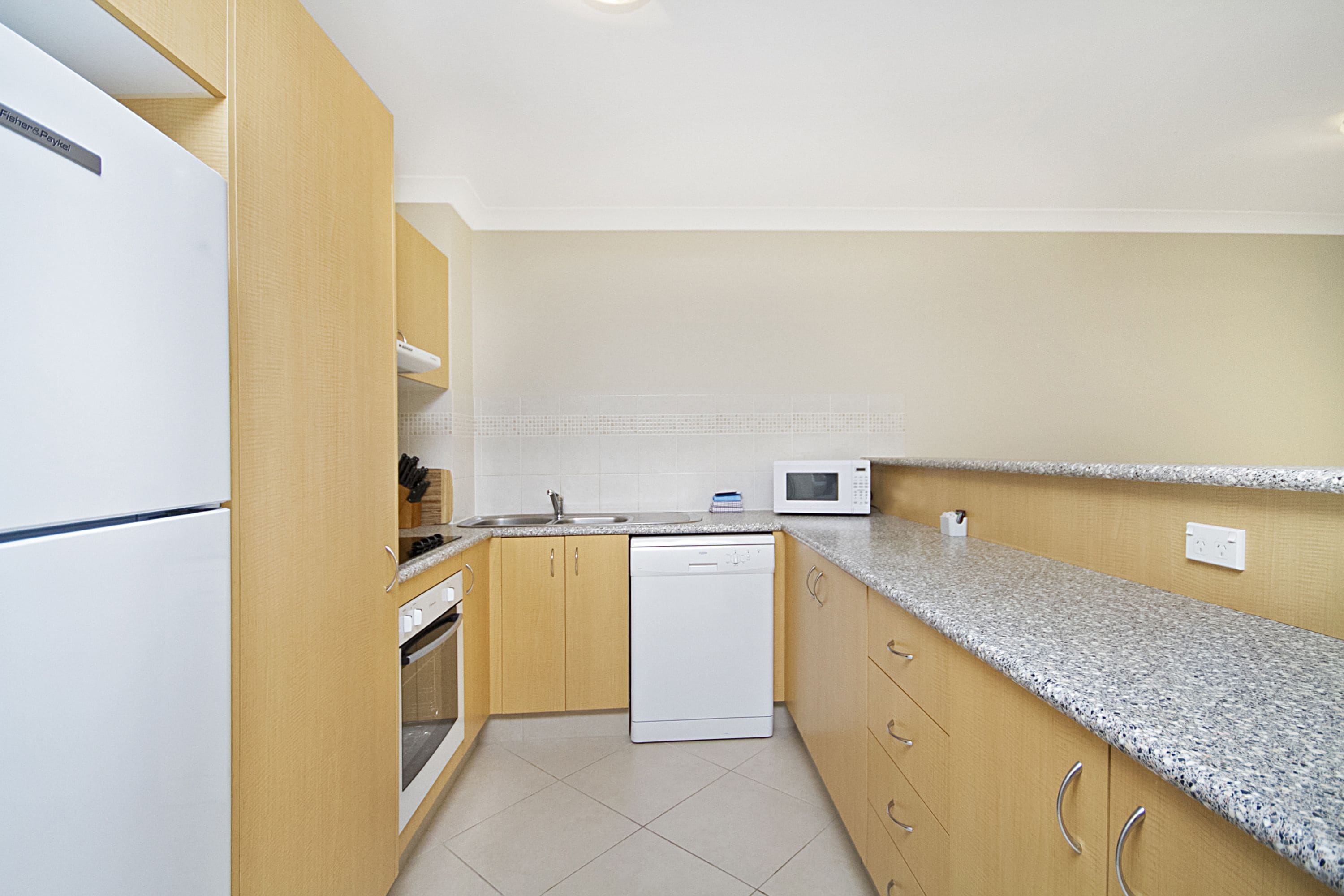 A kitchen with wooden cabinets, a white dishwasher, a microwave, and a stainless steel refrigerator.