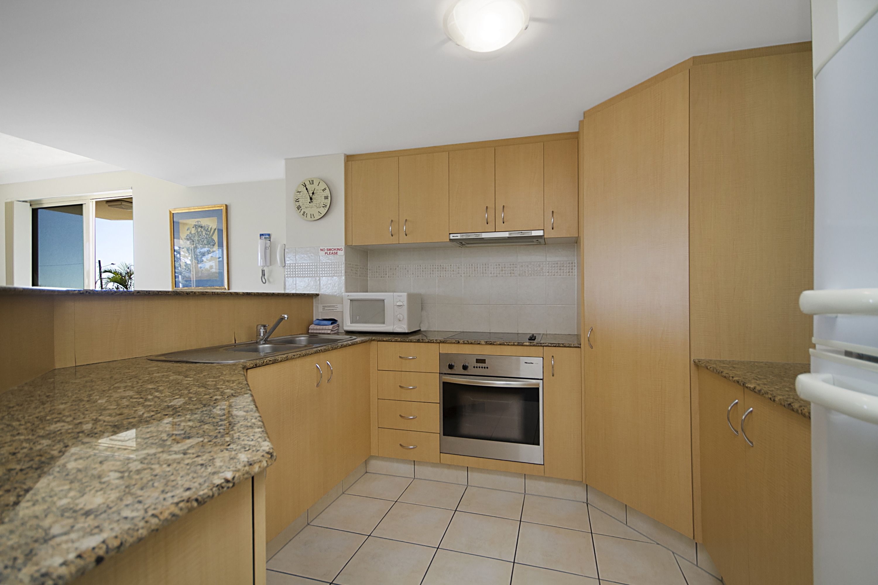 A kitchen with wooden cabinets, a microwave, an oven, and a clock on the wall.