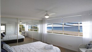 A bedroom with a large bed, a mirror, a view of the beach, and a ceiling fan. - Golden Riviera Beach Resort (Tugun)
