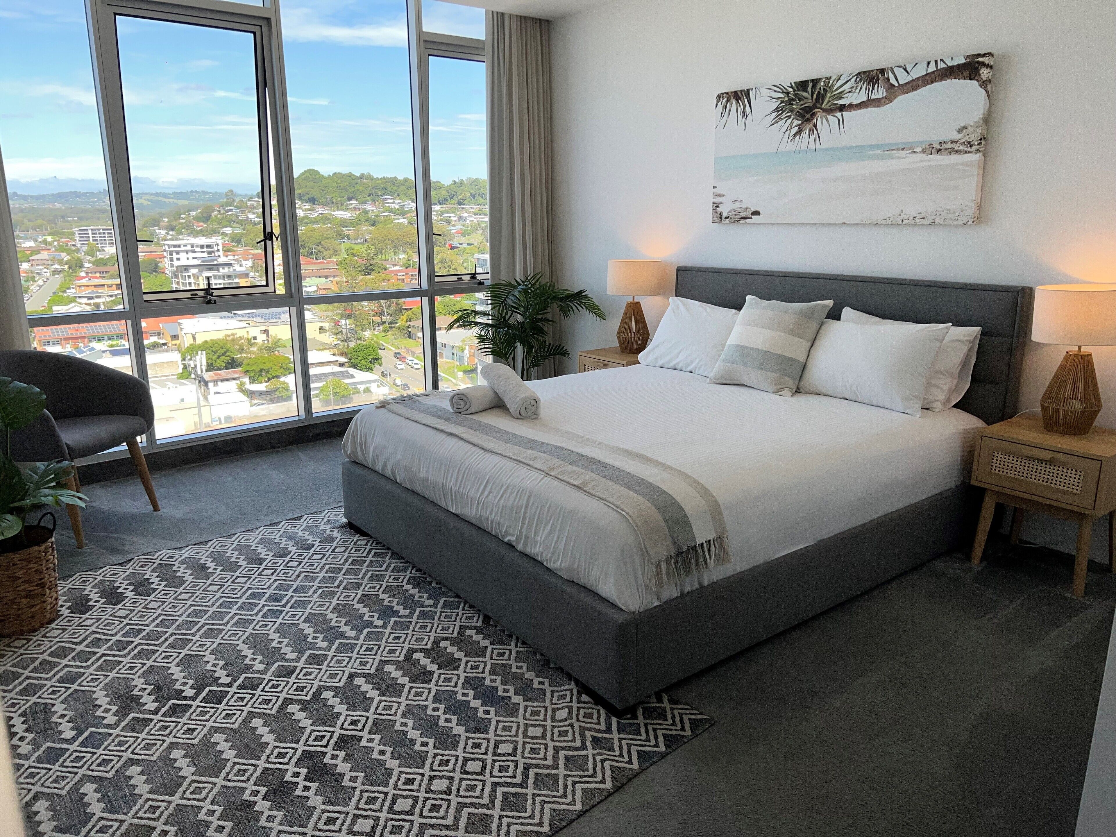 Ein Schlafzimmer mit einem großen Bett, Blick auf die Stadt und einem Gemälde im Strandhausstil.