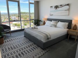 Un dormitorio con una cama grande, vistas a la ciudad y un cuadro con temática marina.