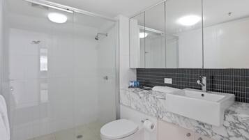 A modern bathroom with a glass-enclosed shower, a white toilet, a sink with a marble countertop, and a large mirror.